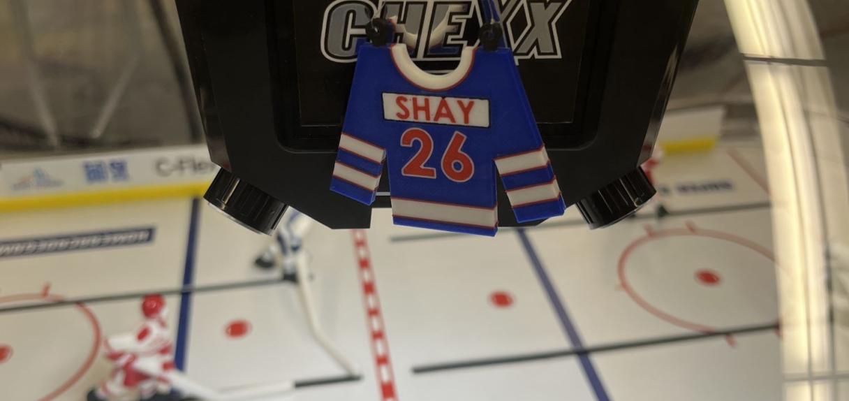 Nahaufnahme des zurückgezogenen Trikots (#26 mit „SHAY“), das in der Hockey-Bubble hängt