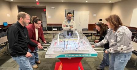 Die Saint-Gobain-Gruppe versammelte sich um den Bubble-Hockey-Tisch und spielte engagiert.